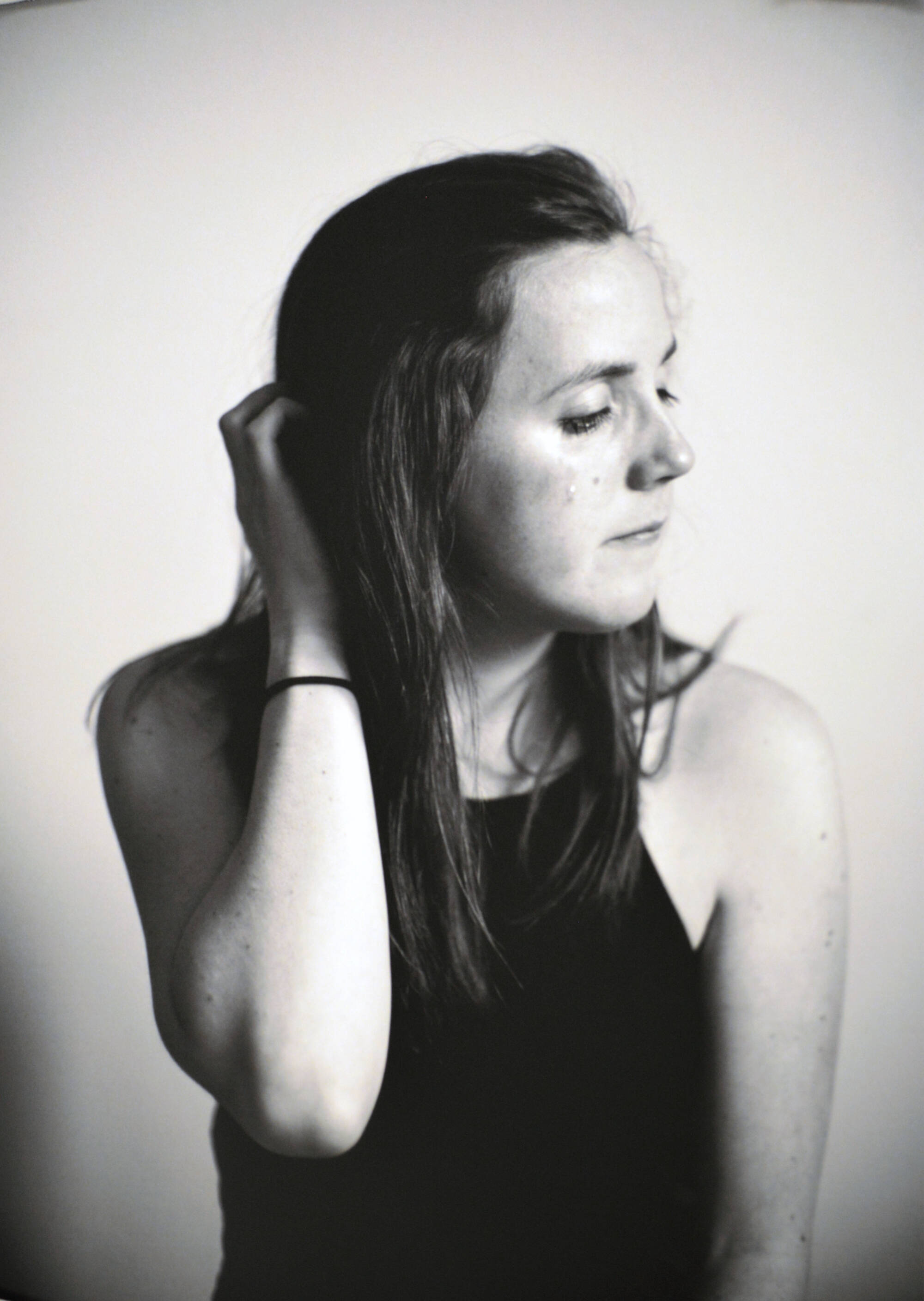 Black and white photograph of a young woman, looking away from the camera, her right hand touching the back of her head.